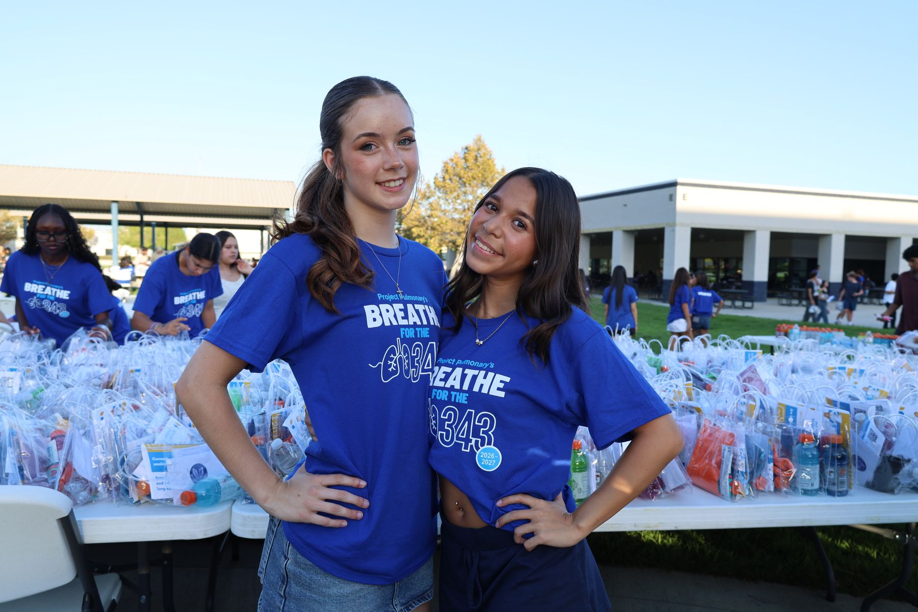 Two volunteers in front of tables of kits