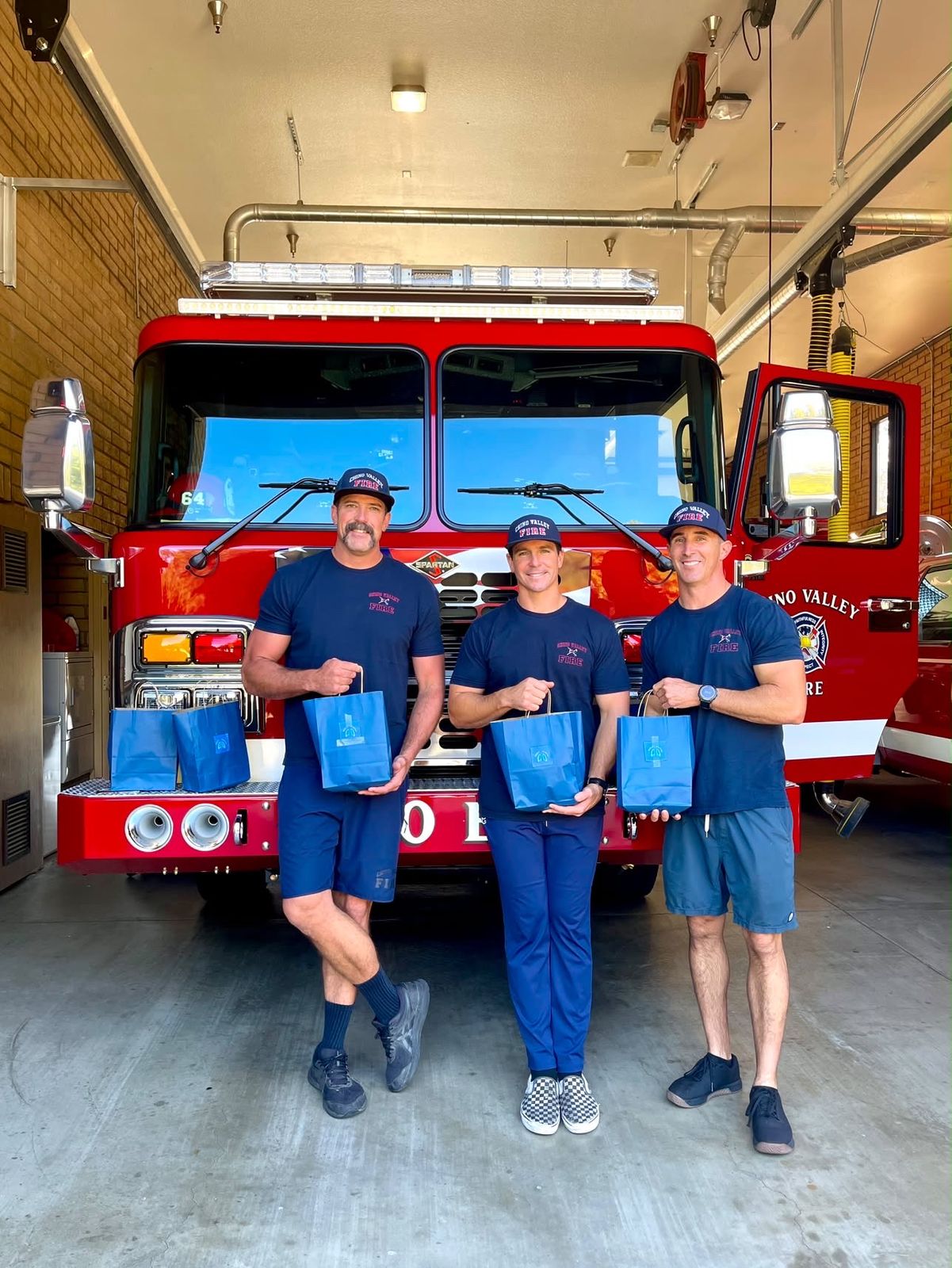 Three firefighters holding gift bags in front of their engine
