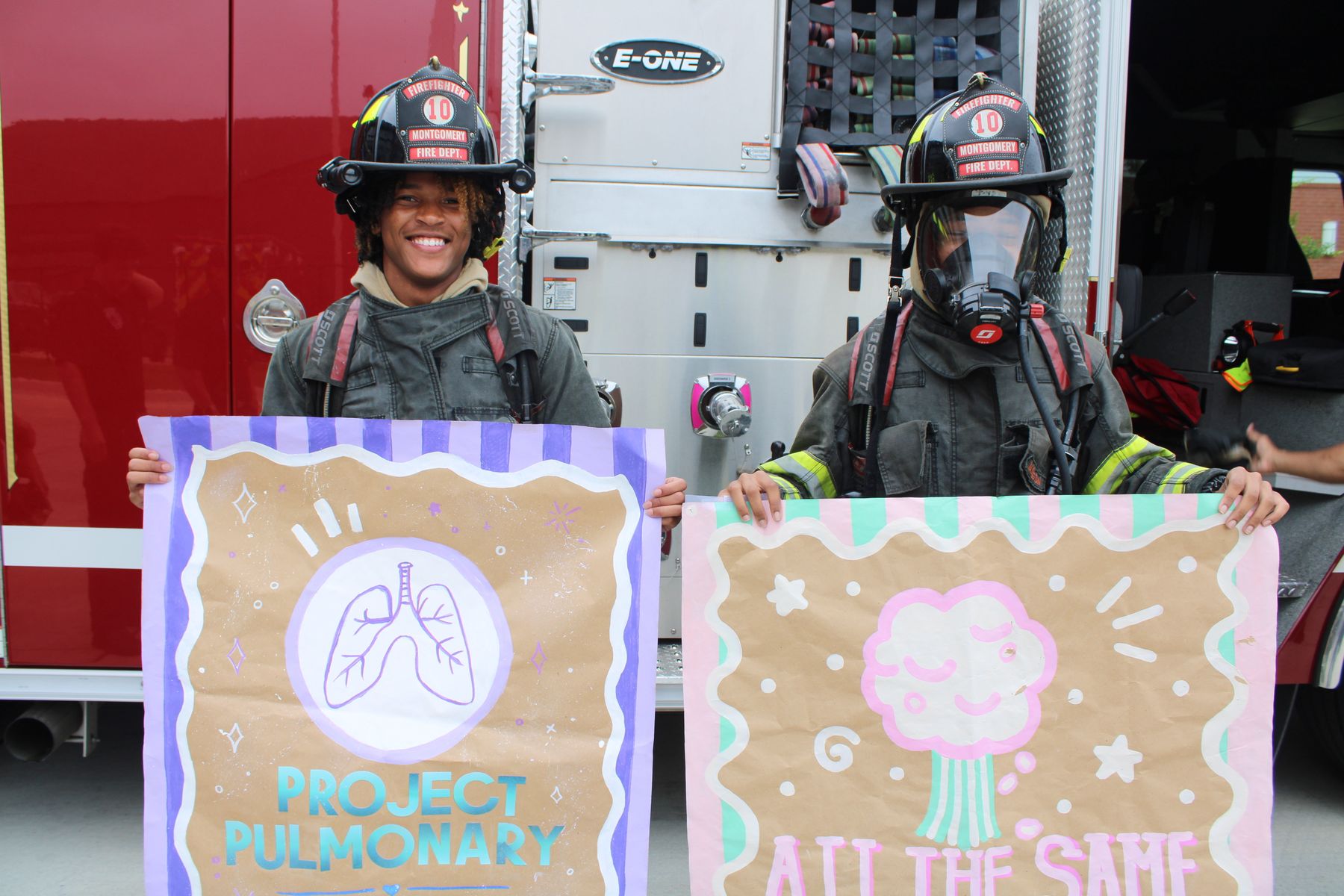 Two firefighters in full turnout gear and helmets holding hand-drawn Letters for Lungs posters